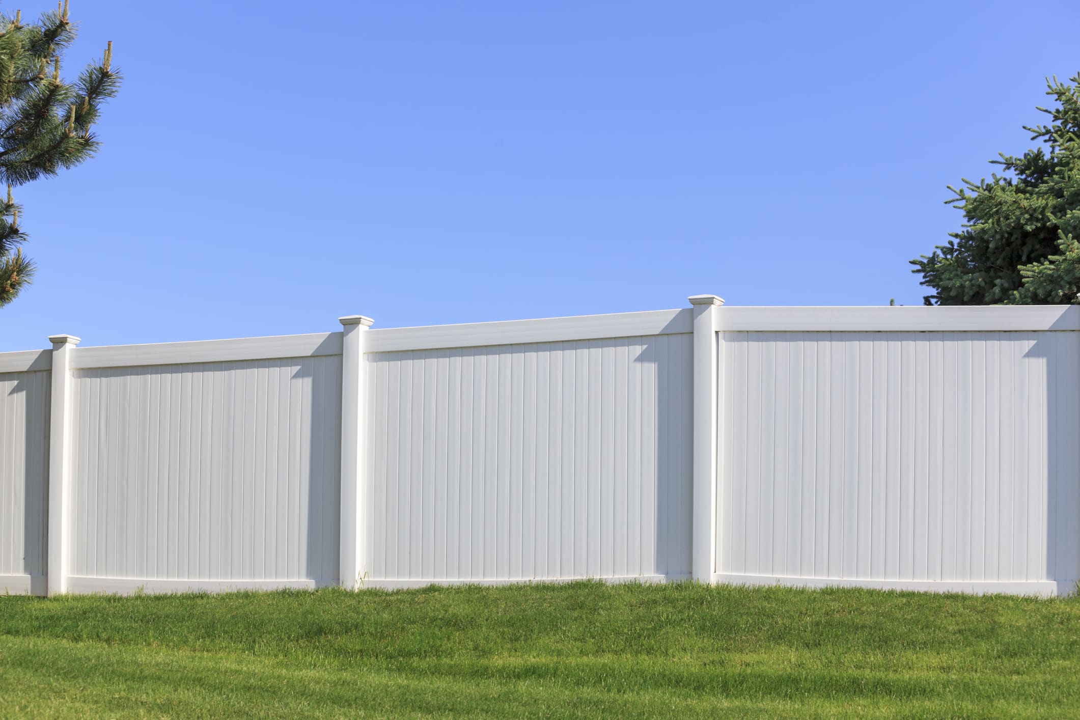 Services 2 A white vinyl fence running across a yard on a bright summers day with blue sky and trees in the background